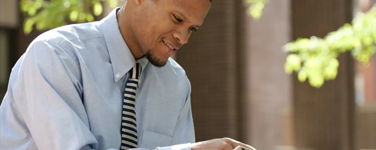 A man in a blue collared shirt and tie using his tablet outside. 