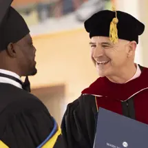 Moody president Mark Jobe in graduation regalia smiling at a graduate