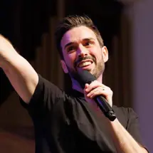 Man smiling with one arm raised while holding a microphone with his opposite hand