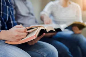 Two people sitting down together read their Bibles. 